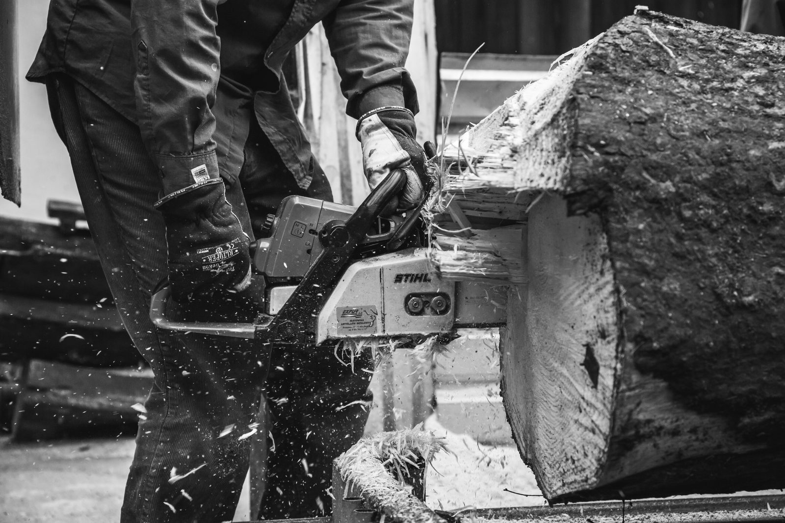 A person cutting a log with a chainsaw, sawdust in the air