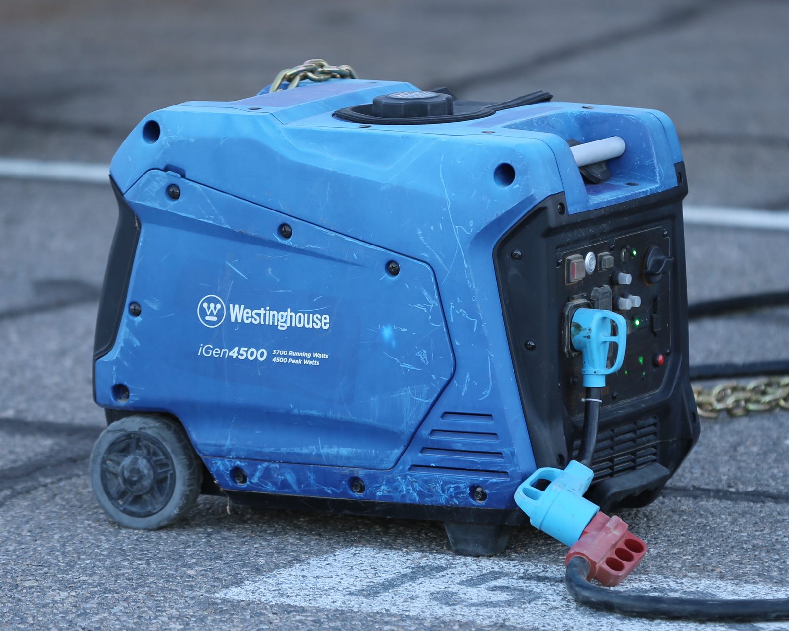 A blue Westinghouse iGen4500 portable inverter generator running on pavement with a power cord plugged into its outlet panel