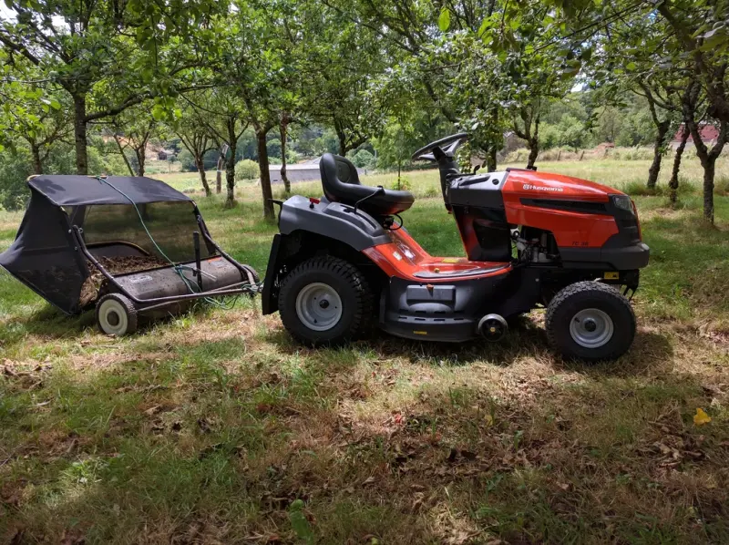 A green riding lawn tractor with a sweeper attachment on a lawn