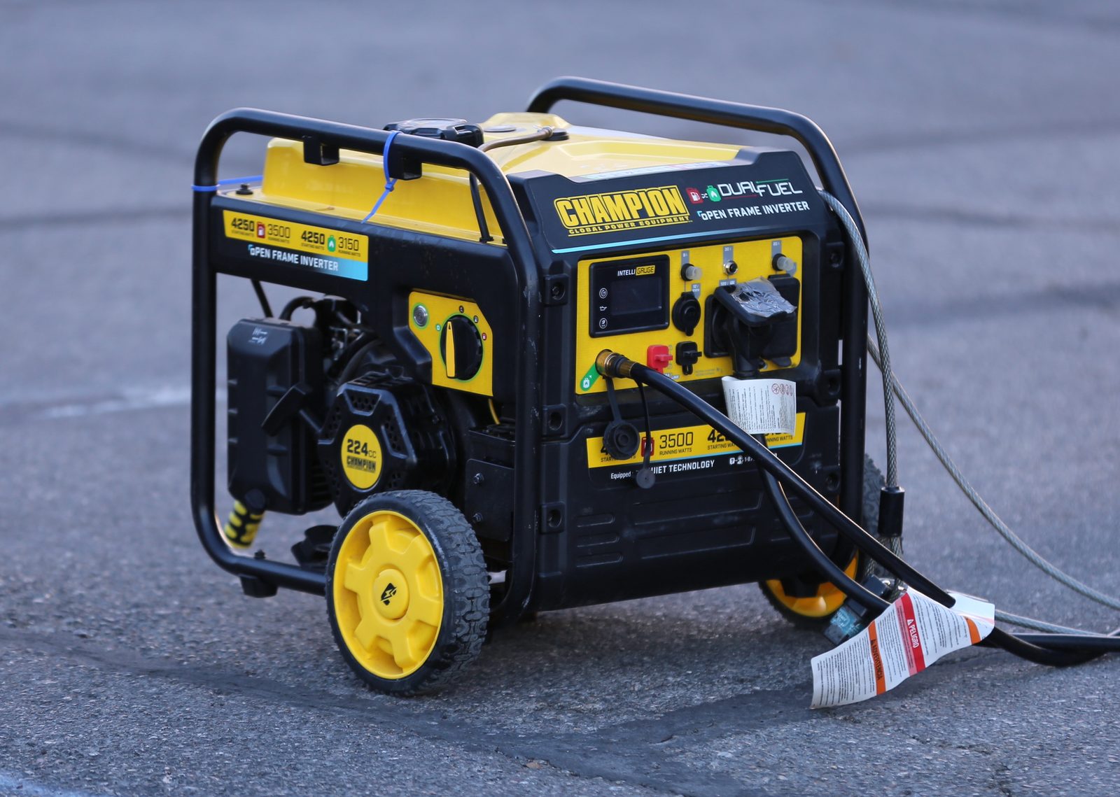 A yellow and black Champion 4250-watt dual-fuel open-frame inverter generator with a fuel hose attached, standing on pavement