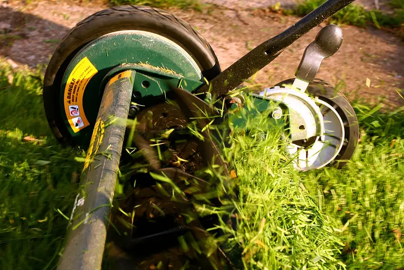 A person pushing a walk-behind mower across a green lawn