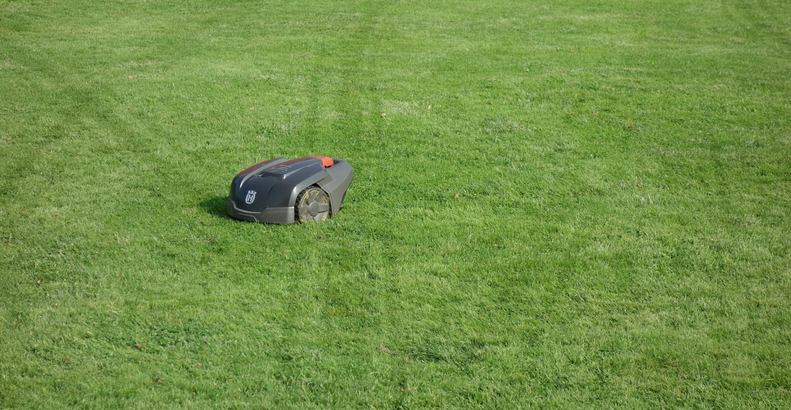 A robotic lawn mower crossing a lawn with visible wheel track marks in the grass