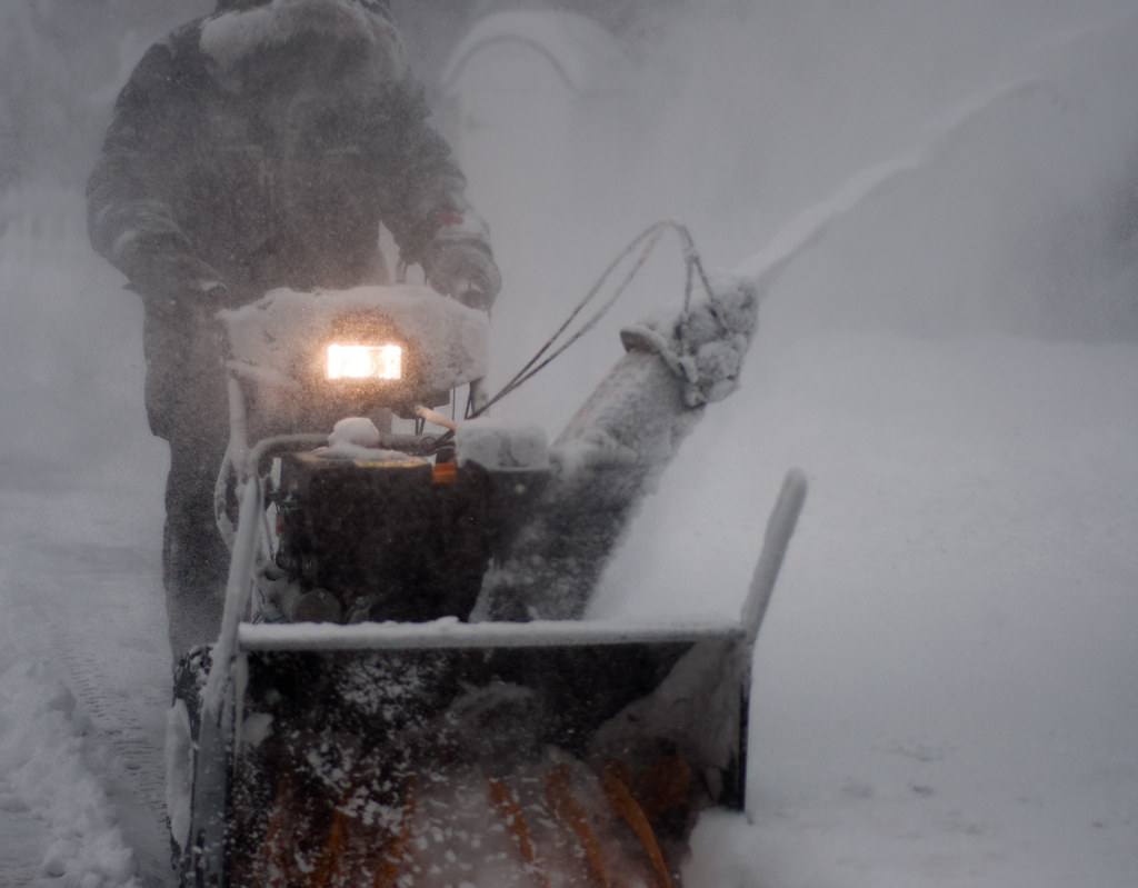 A two-stage snow blower clearing a snow-covered driveway