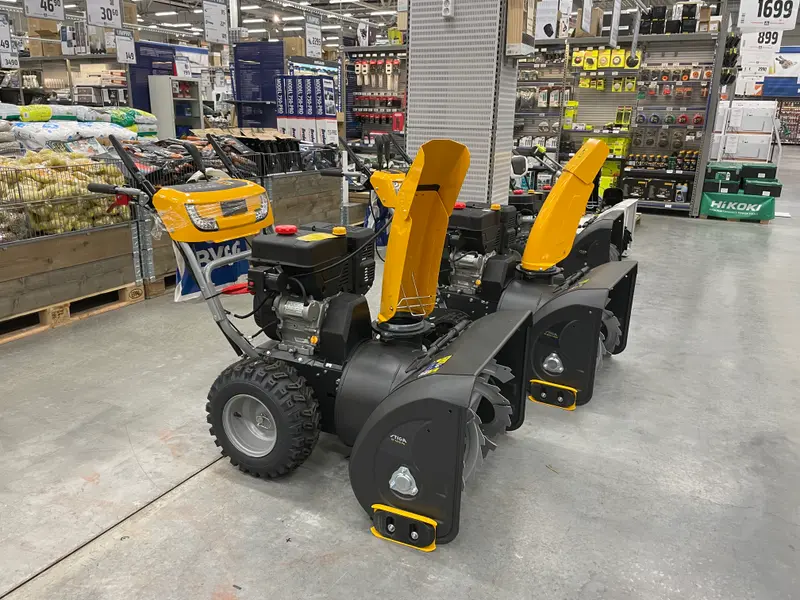 Two gas two-stage snow throwers on display in a hardware store beneath price signs