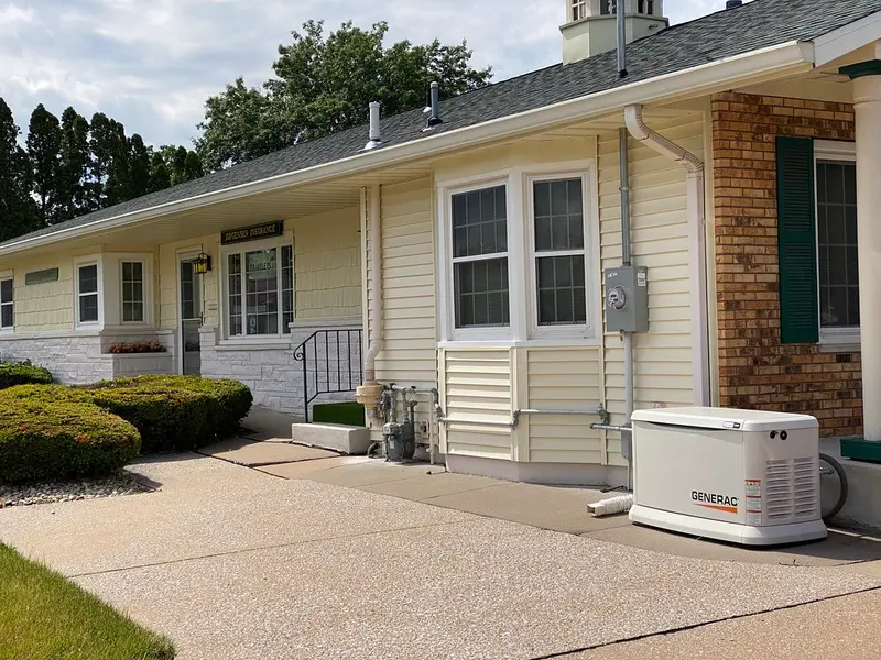 A white Generac standby generator installed beside a house, connected to gas piping and an electric meter